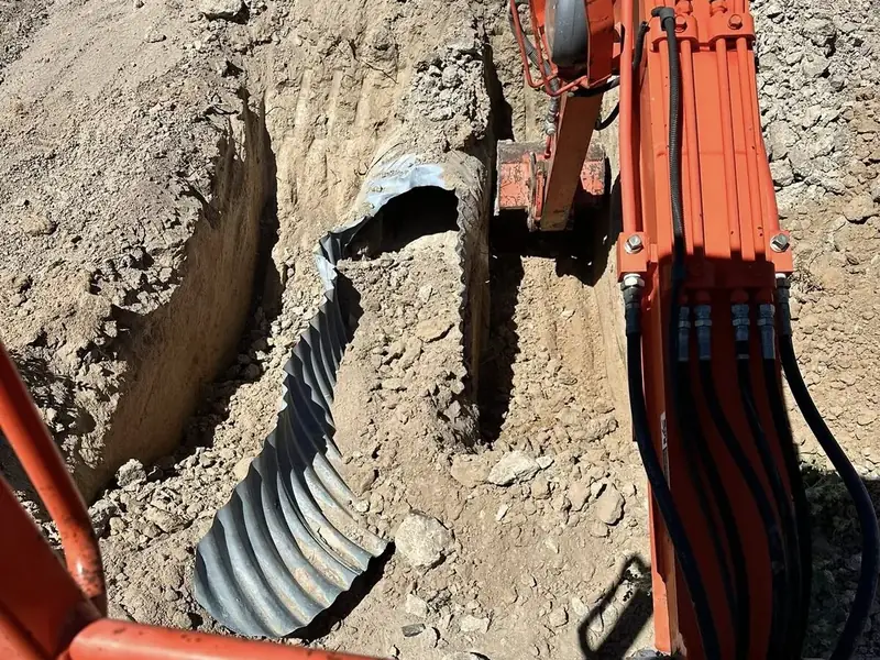 Excavator arm placing a corrugated culvert pipe in a trench