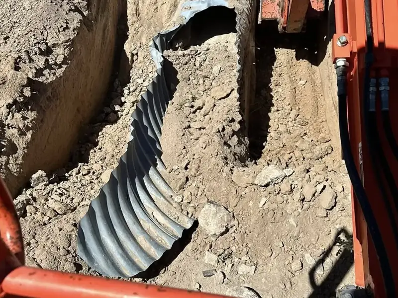 Corrugated culvert pipe being set into a freshly dug drainage trench