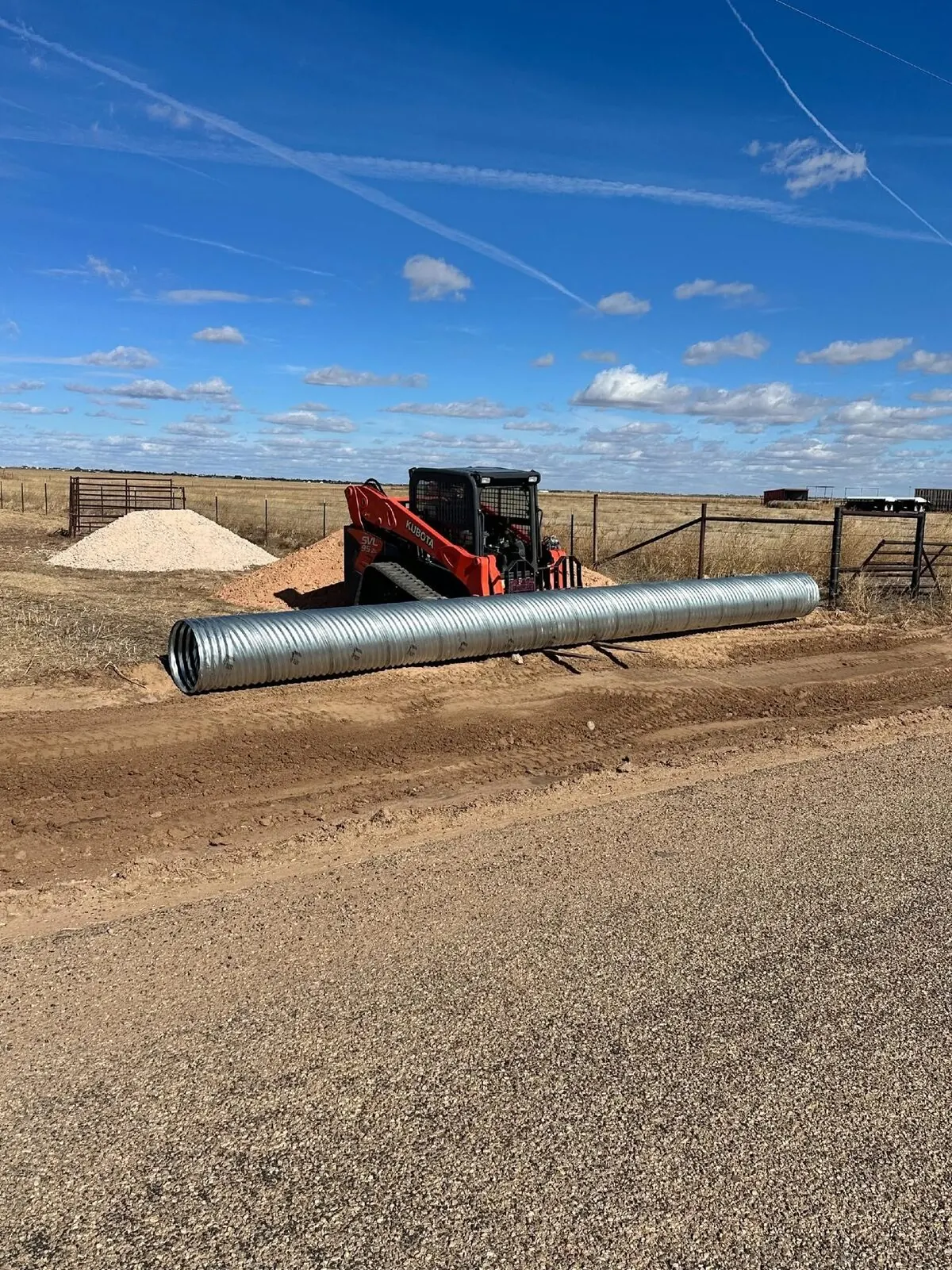 Skid steer delivering a culvert pipe on a ranch road