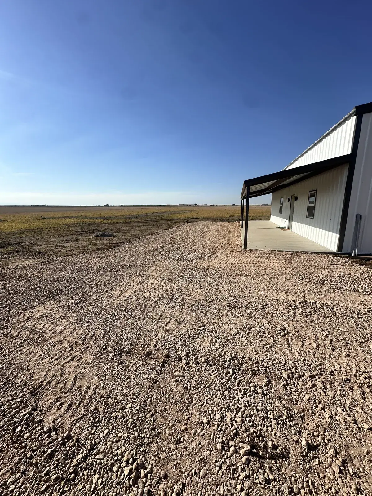 A finished gravel driveway and pad wrapping around a metal shop building on the open Texas Panhandle plains