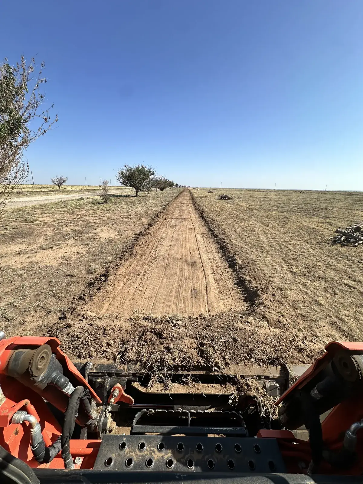 A box blade grading a new dirt ranch road across a flat Texas Panhandle field