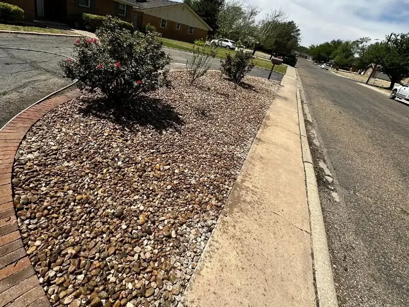 Decorative river-rock landscaping bed with brick edging along a residential drive